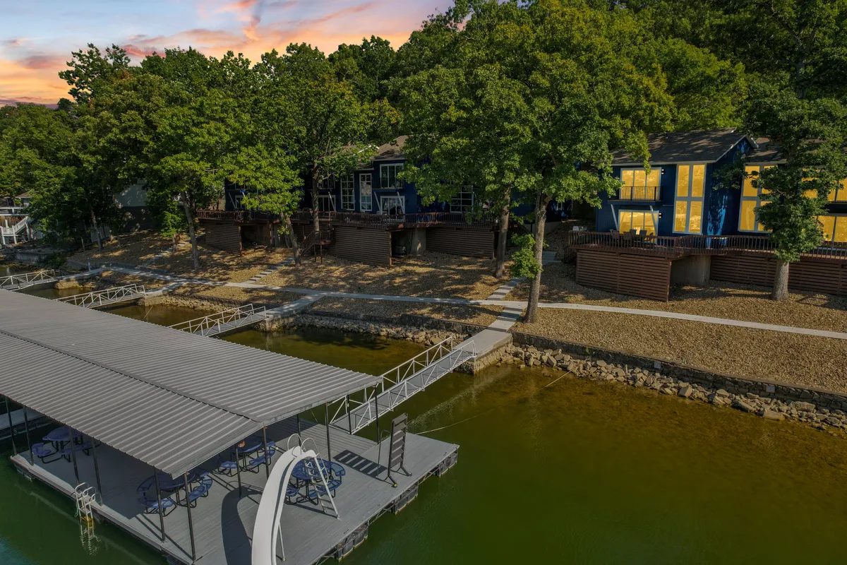 A peaceful dock stretches into the lake, with waterfront cabins and trees lining the shore. The sunset sky glows warmly, hinting at evening tranquility and romantic experiences at dusk. The setting invites couples to enjoy quiet evenings or gather on the dock.