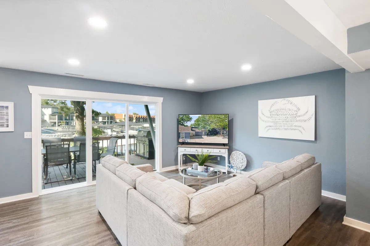 This image showcases a spacious open-plan living area featuring a large sectional sofa, flat-screen TV, decorative wall art, and expansive glass sliding doors that let in natural light and offer glimpses of the outdoors. The room feels airy, comfortable, and perfectly set for relaxation or socializing.