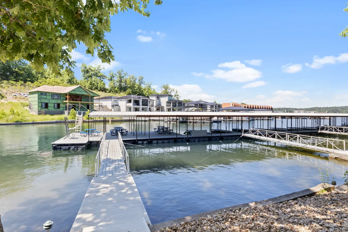 A welcoming dock and waterfront area framed by greenery, with buildings visible in the background. The scene is tranquil and suggests a place for relaxing by the water, fishing, or sitting with pets after a day of activity.