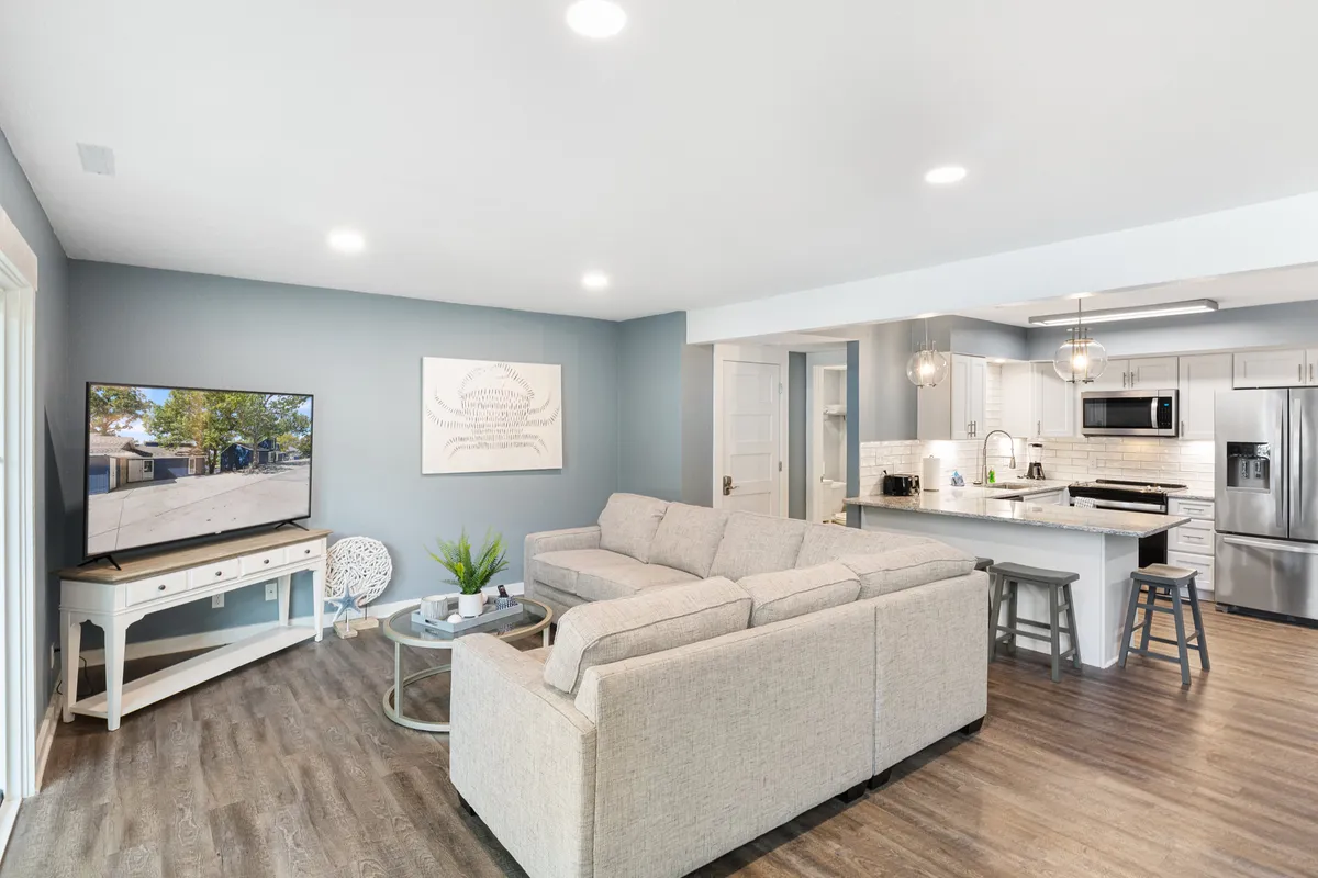 A bright, open interior with a sofa, television, kitchen area, and decorative artwork. The space appears clean, cozy, and organized, suggesting a comfortable spot for both guests and their pets. The layout allows for easy movement between rooms and a welcoming environment for responsible pet owners.