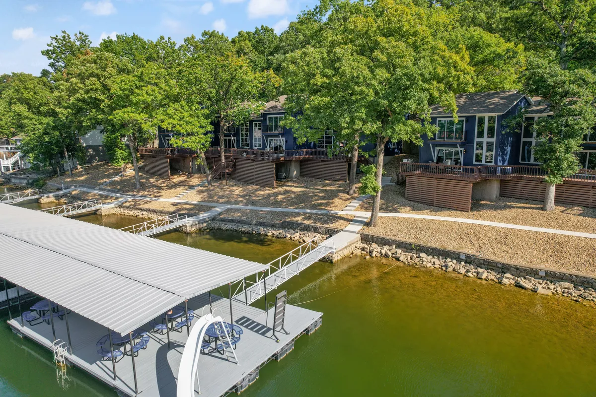 An exterior view highlighting a dock, nearby waterfront cabins, trees, and a pathway. The scene radiates tranquility and direct connection to lakeside nature, with open space ideal for pet walks. The gentle sunset and water views reinforce the peaceful and inviting environment.