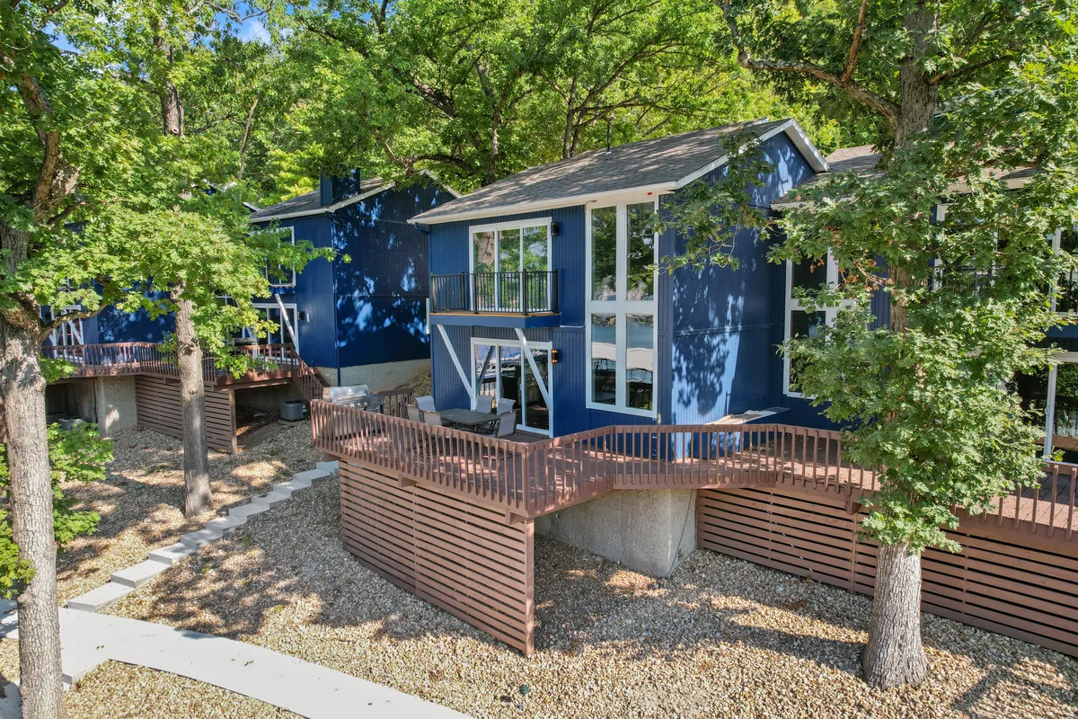 This image features the blue exterior of the condo, with large windows letting in natural light, a wooden deck with railings, and surrounding trees. The outdoor deck area is spacious and inviting, perfect for relaxing or spending time with pets. The setting suggests opportunities for pet-friendly activities and easy access to outdoor spaces.