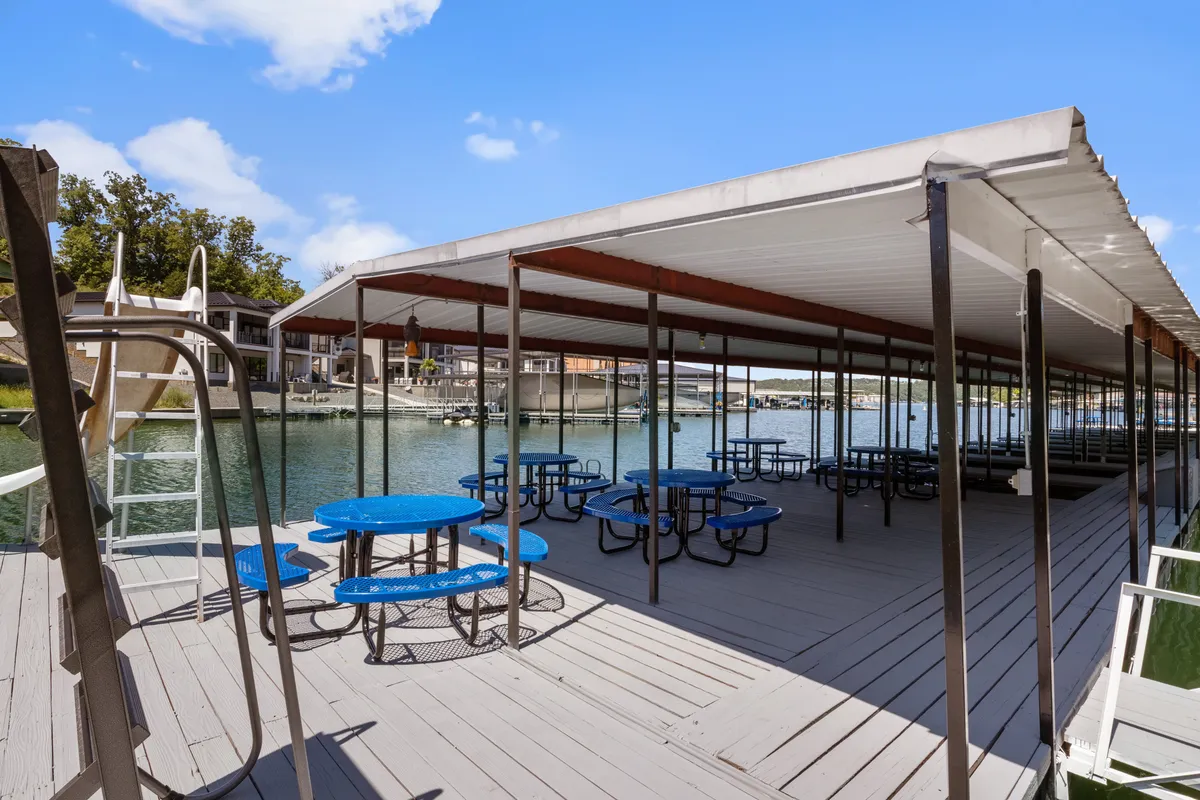 Picnic tables sit near the water's edge, with a view of boathouses, a swimming ladder, and the broad waterfront. The setting feels casual yet inviting, suggesting shared meals, outdoor fun, and intimate lakeside gatherings.