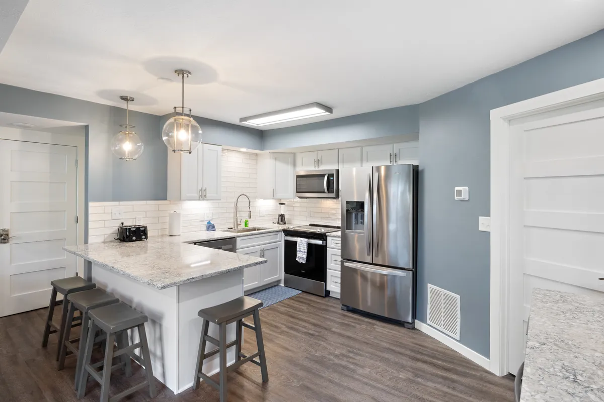 This image features a modern kitchen with granite countertops, stainless steel appliances, and pendant lighting. The open layout suggests an inviting space suitable for cooking, gathering, and entertaining. The kitchen island provides ample workspace and seating for family or guests to participate in meal preparation.