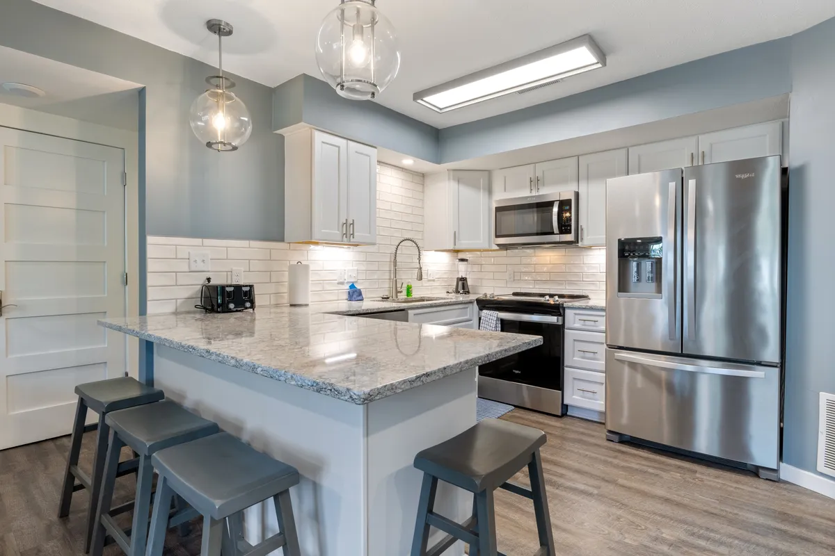 A contemporary kitchen spotlighting a large island, granite countertops, pendant lights, and stainless steel appliances. The space is designed for both functionality and social interaction, with seating at the island for casual dining or participating in meal prep.