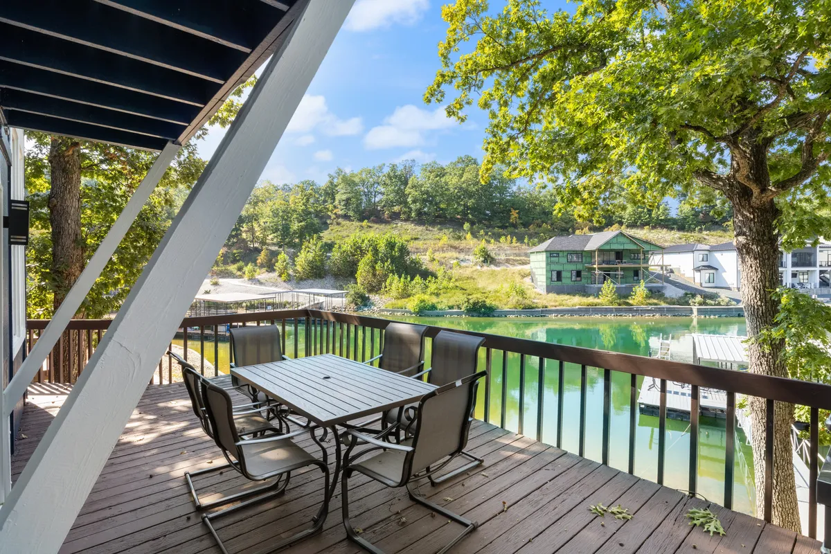 The image showcases a serene outdoor patio with a dining table and chairs set against the backdrop of tranquil lake waters and lush, green trees. The scene captures the peacefulness of the cove, with inviting spaces for outdoor dining and relaxation, and hints at the opportunities for sunrise views and evening stargazing.