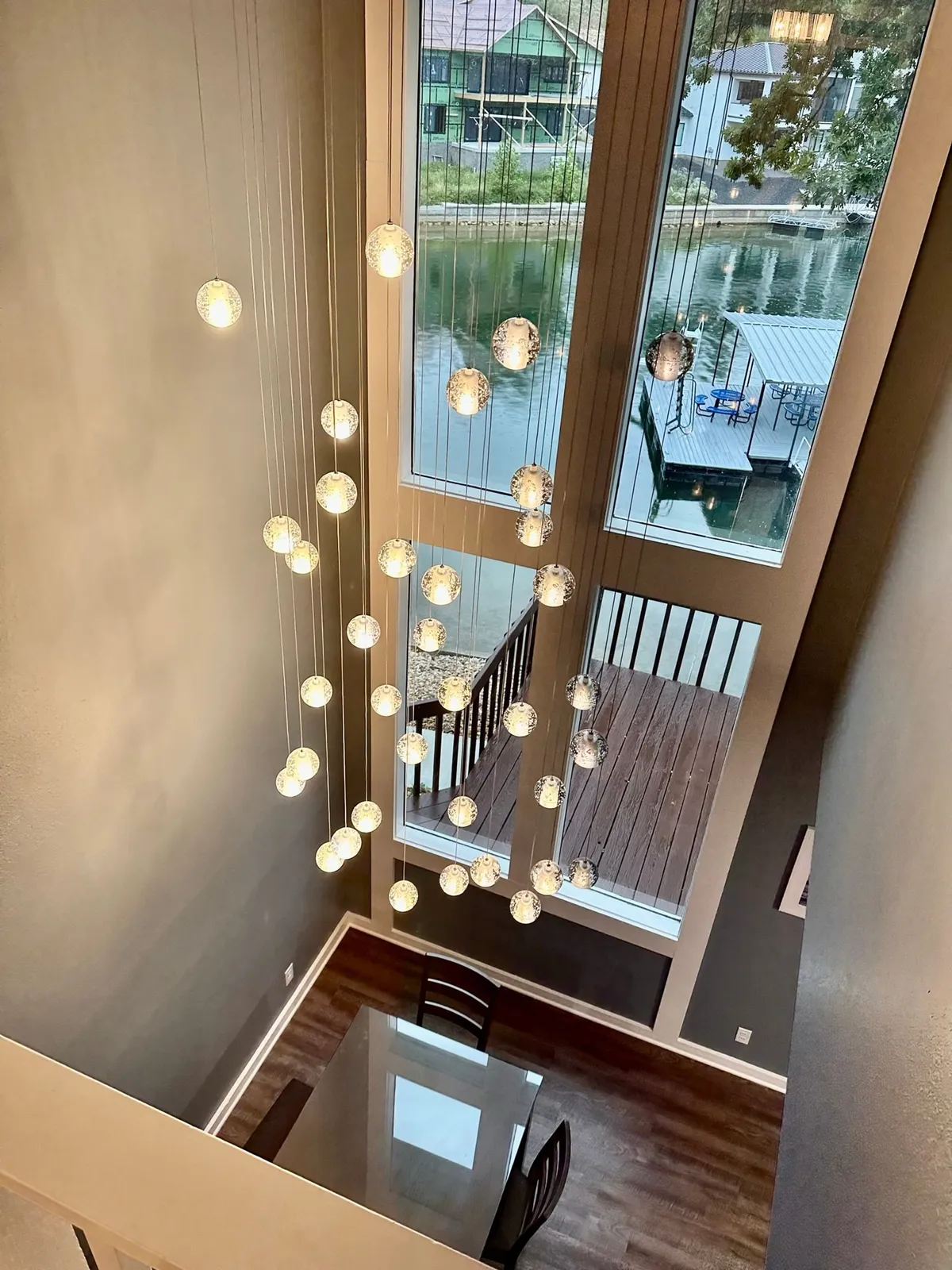 A beautifully set dining table adjacent to floor-to-ceiling windows overlooking the water. Suspension lights add a warm glow, and the space feels both serene and inviting—ideal for dinners with a view of the cove.