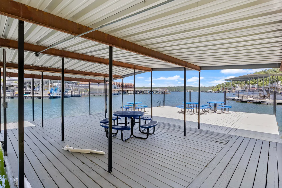 An inviting exterior scene featuring picnic tables overlooking a picturesque waterfront and pier, with open skies and gentle light. The setup suggests an ideal spot for socializing, casual outdoor meals, or planning the next group adventure.