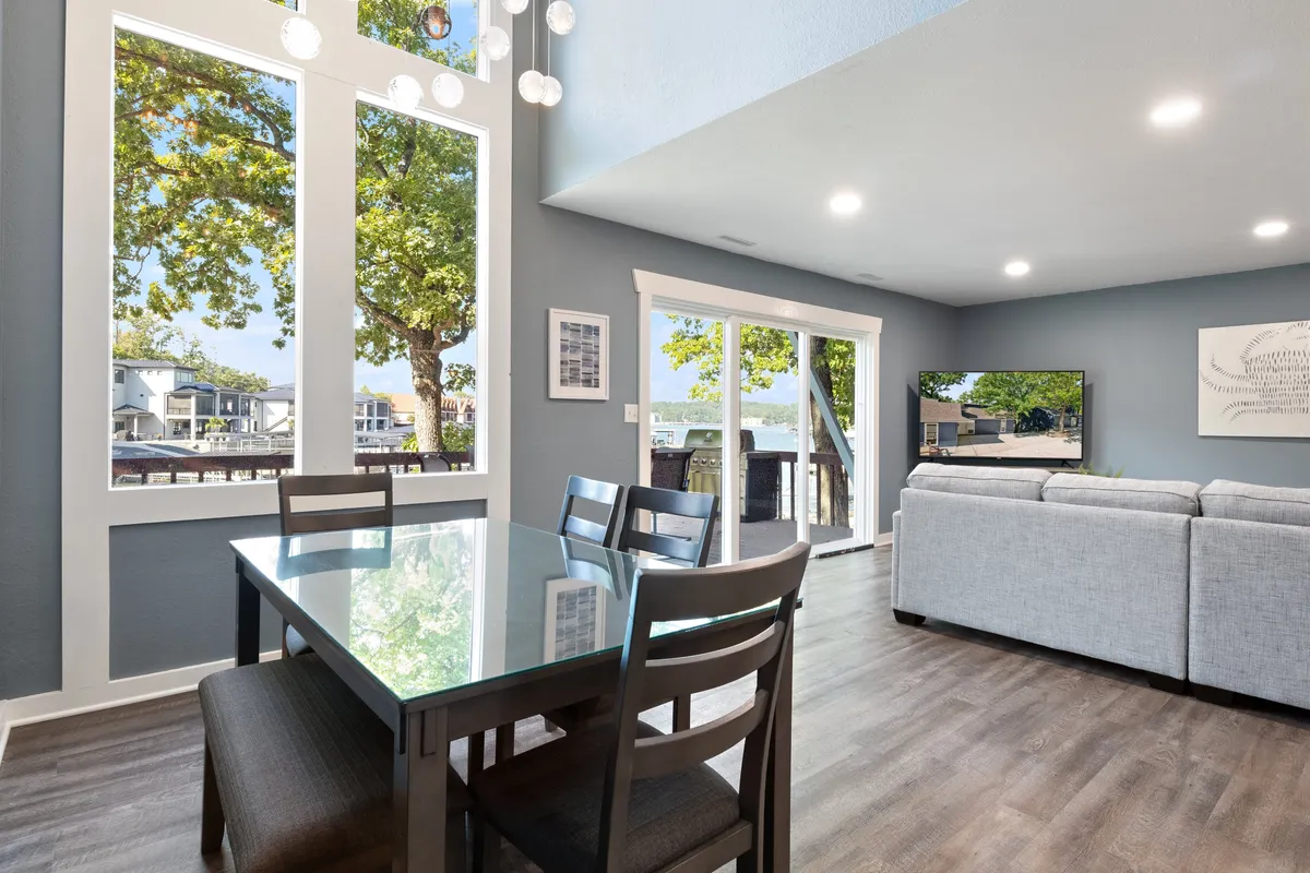 A bright living and dining area with large windows, a welcoming dining table, comfortable sofa, and TV. Sunlight pours in, illuminating the communal spaces and providing lovely views that set the stage for gathering and shared experiences.