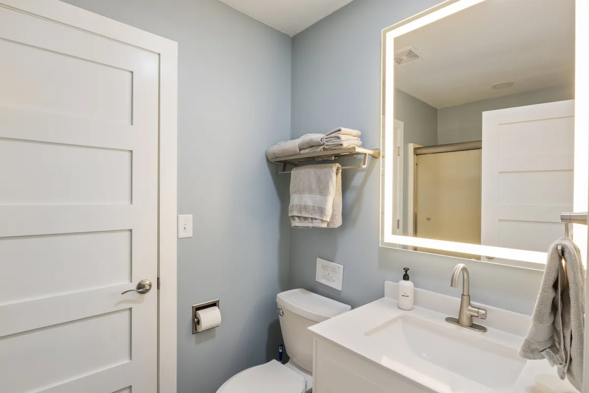A calm, modern bathroom featuring a vanity with a sink, a large mirror, towels neatly arranged on a rack, and a toilet. The serene color palette and tidy organization contribute to a spa-like feel, ideal for relaxation and self-care.